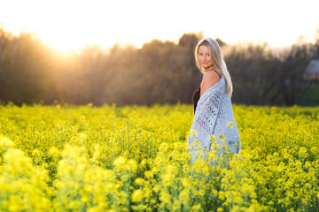 A pretty girl in a field of yellow flowers with a sunflair behind her during sunset