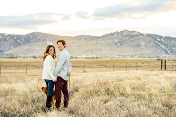 A couple in a field with their dog and mountians in the background